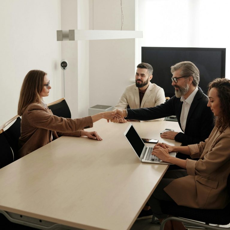 Business professionals engaging in a handshake across a conference table, signifying successful collaboration.